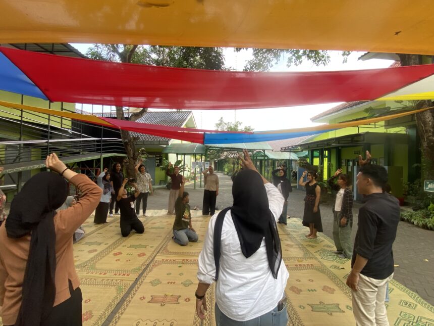 Group of people standing and raising hands under colorful fabric canopies in a courtyard.
