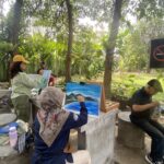 Outdoor painting workshop with people painting on easels among trees and plants in a garden setting.
