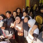 Crowded indoor event with many people seated shoulder to shoulder, some wearing hijabs, against an orange wall.