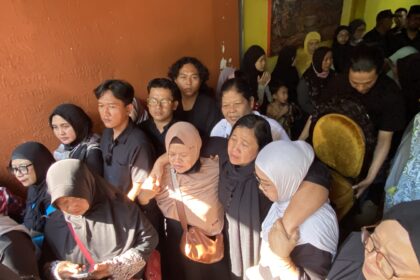 Crowded indoor event with many people seated shoulder to shoulder, some wearing hijabs, against an orange wall.