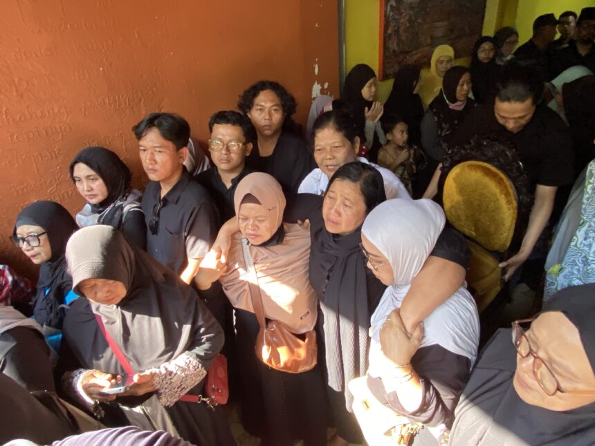 Crowded indoor event with many people seated shoulder to shoulder, some wearing hijabs, against an orange wall.