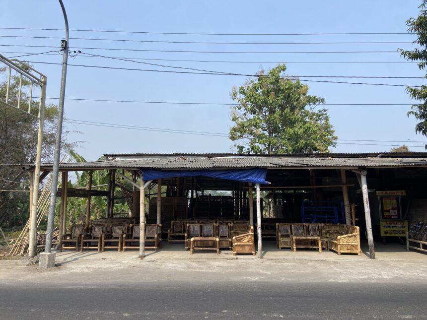 Open-air furniture workshop with many wooden bamboo chairs under a corrugated roof, power lines overhead.