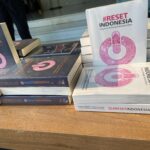Stack of books titled '#RESET INDONESIA' with a pink circular logo on the white cover, arranged on a table.