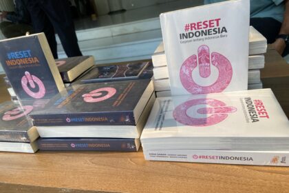 Stack of books titled '#RESET INDONESIA' with a pink circular logo on the white cover, arranged on a table.