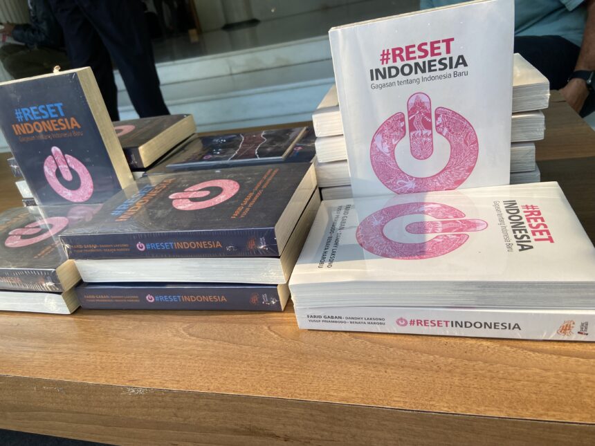 Stack of books titled '#RESET INDONESIA' with a pink circular logo on the white cover, arranged on a table.