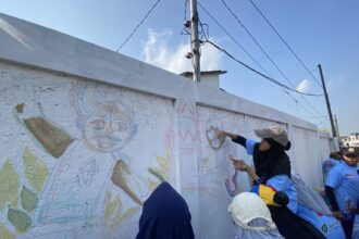 People in blue outfits painting a colorful mural on a white wall outdoors under a clear blue sky.