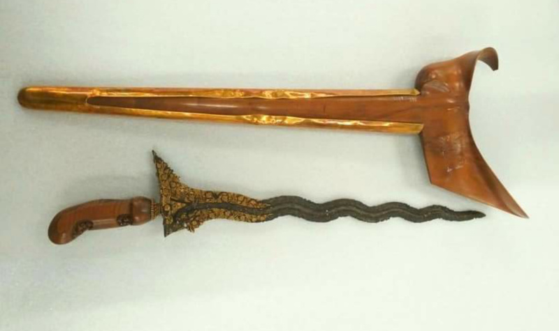 Ornate dagger with a wavy black blade and gold filigree guard beside a curved brown sheath.