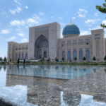 Islamic mosque with a turquoise blue dome and ornate tilework, its arches facing a reflecting pool that mirrors the building's facade.