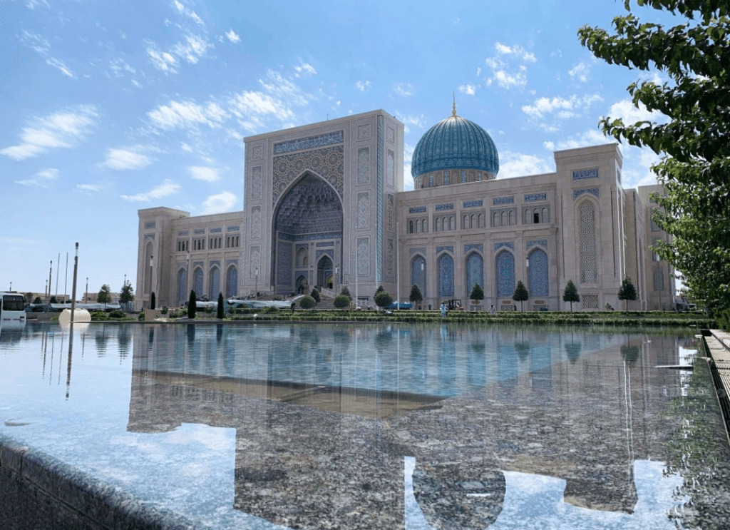 Islamic mosque with a turquoise blue dome and ornate tilework, its arches facing a reflecting pool that mirrors the building's facade.