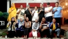 Group of people posing on a stage, some making hand signs, smiling at the camera.