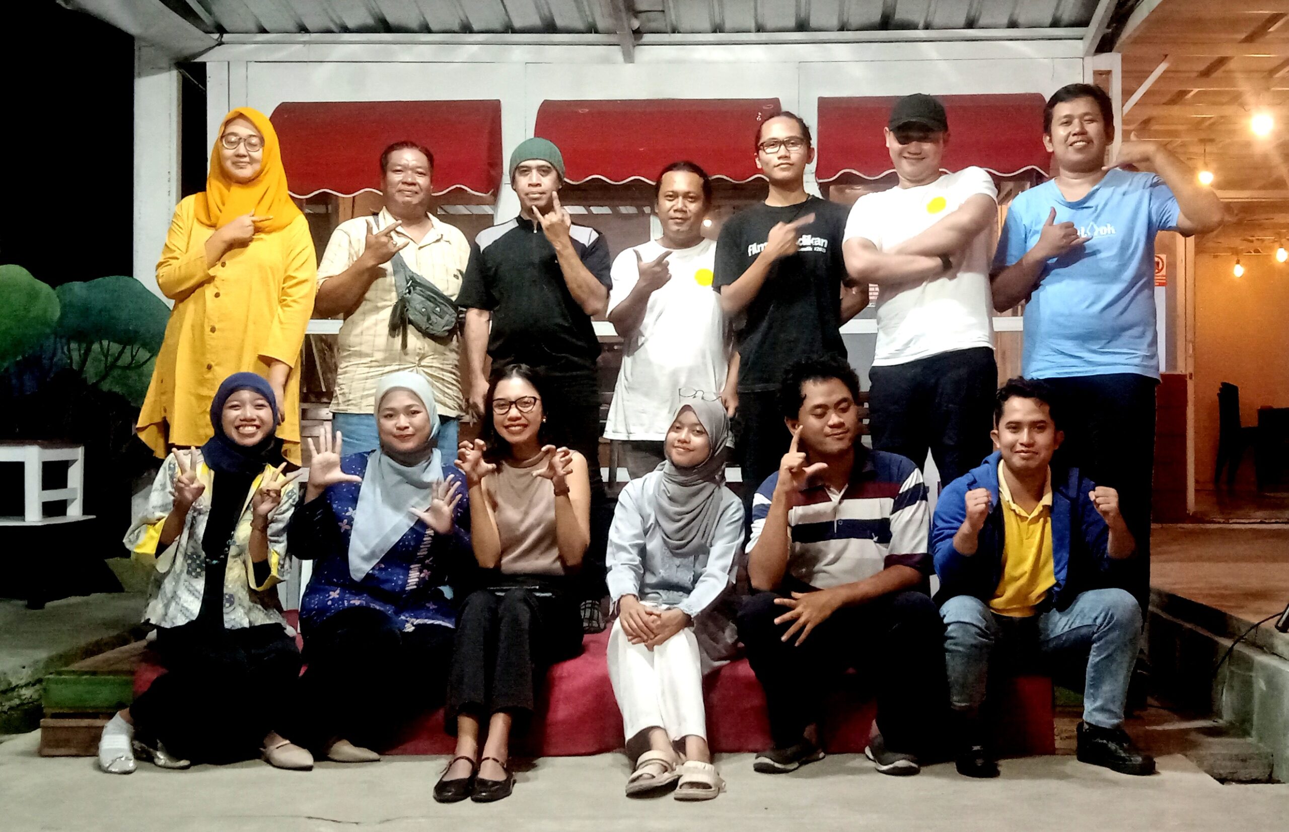 Group of people posing on a stage, some making hand signs, smiling at the camera.
