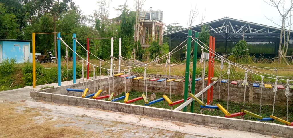 IMG_20260612_150227 - Mabur.co Outdoor obstacle course with colorful planks and ropes suspended between tall posts in a yard.