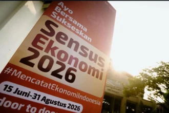 Tilted orange banner announcing 'Sensus Ekonomi 2026' with dates and hashtag #MencatatEkonomiIndonesia, sunlit outdoor setting.