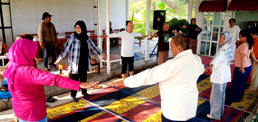 People of diverse ages form a circle with arms extended, participating in a group stretch on a colorful mat.