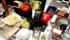 Table full of vintage electronics and knickknacks at a flea market stall, including red payphone, old phones, magazines, and dishes.
