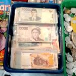 Stacks of Indonesian rupiah banknotes in a blue tray beside a pile of coins on a market counter.