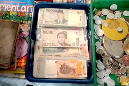 Stacks of Indonesian rupiah banknotes in a blue tray beside a pile of coins on a market counter.
