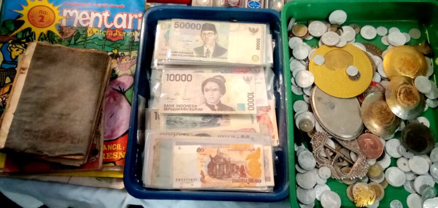 Stacks of Indonesian rupiah banknotes in a blue tray beside a pile of coins on a market counter.