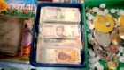 Stacks of Indonesian rupiah banknotes in a blue tray beside a pile of coins on a market counter.