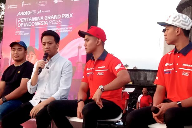 Panel of four men seated on stage during a MotoGP event, with a pink banner in the background reading 'PERTAMINA GRAND PRIX OF INDONESIA 2026'. One man speaks into a microphone while the others wear red Honda-branded shirts or casual attire.