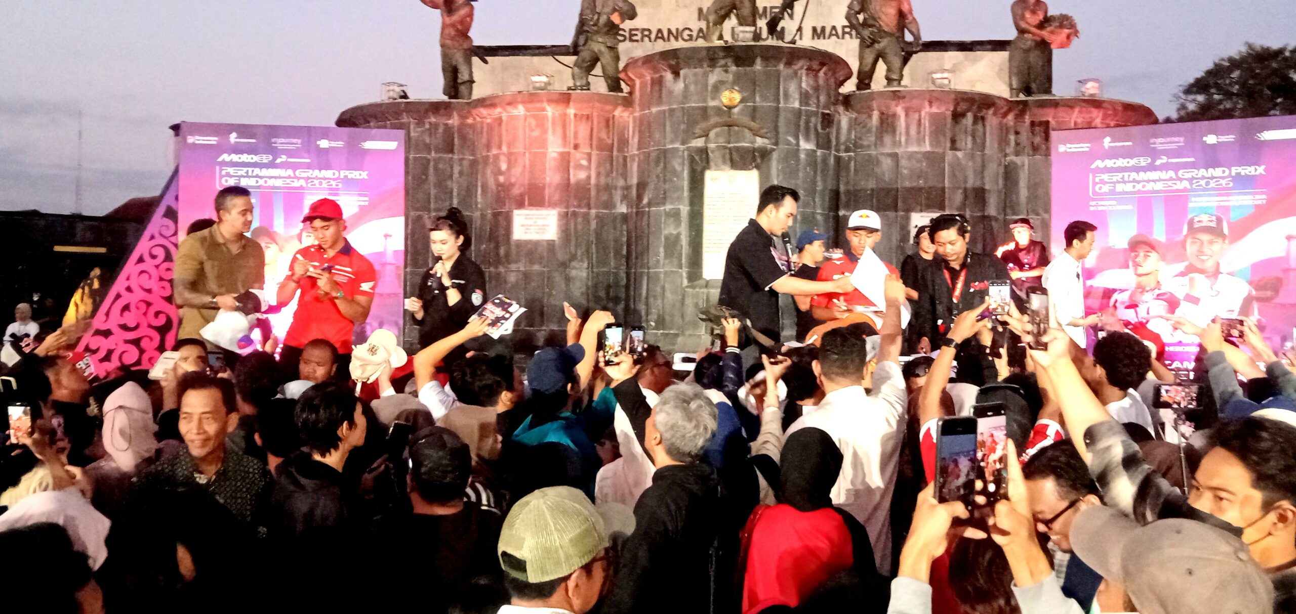 Crowd watches a racing event on a marble stage with banners reading Pertamina Grand Prix of Indonesia 2016; speakers and camera phones abound.