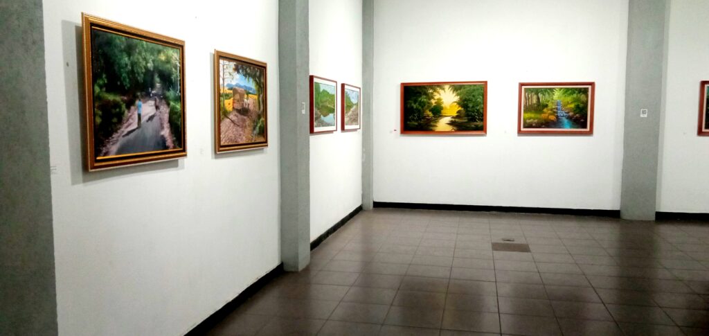 Gallery hall with several landscape paintings in wooden frames along white walls.