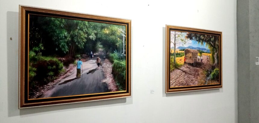 Two framed paintings on a white gallery wall; left image shows a forest path with people walking, right image shows a rural dirt road with a wagon drawn by oxen.