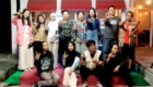 Group of young people posing on a stage with red awnings, making L-shaped hand gestures and smiling.