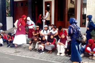 Group of children with backpacks sitting on steps outside a building, waiting or resting.
