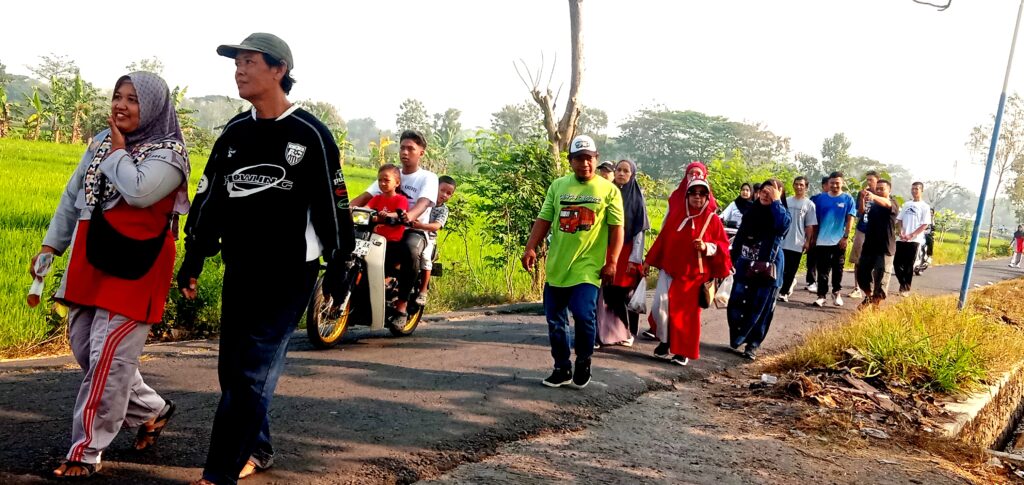 A diverse group of people walking along a rural road at dusk, some in bright clothing, chatting as they proceed in a single file line.
