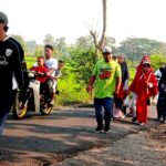 A diverse group of people walking along a rural road at dusk, some in bright clothing, chatting as they proceed in a single file line.