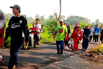 A diverse group of people walking along a rural road at dusk, some in bright clothing, chatting as they proceed in a single file line.