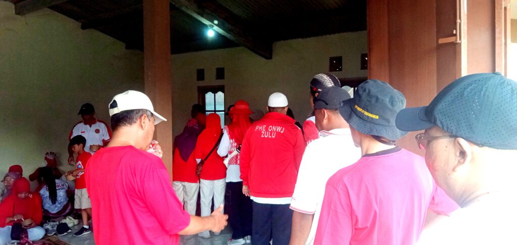 Group of people in red clothing inside a dim hall, some seated along the left wall and others standing in line.
