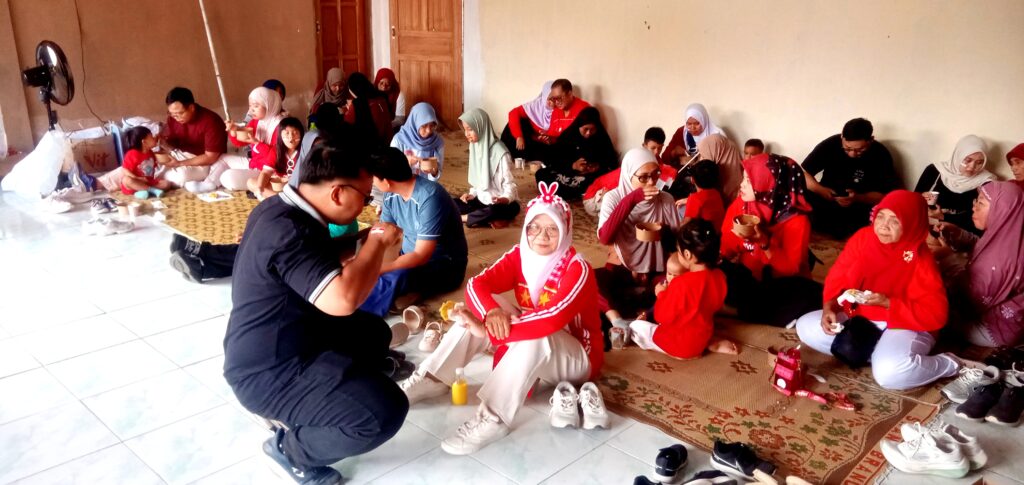Group of people seated on the floor inside a room, sharing bowls of food at a community gathering.