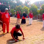 Group of people in red and white outfits playing a croquet-style game on a dusty ground while others watch at a festival, with bunting overhead.