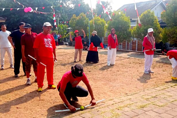 Group of people in red and white outfits playing a croquet-style game on a dusty ground while others watch at a festival, with bunting overhead.