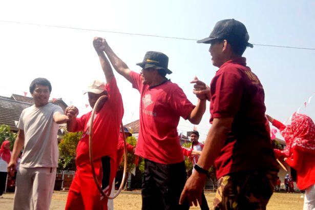 Group of people in red shirts dancing or celebrating outdoors at a festive event, with bunting flags and onlookers in the background.