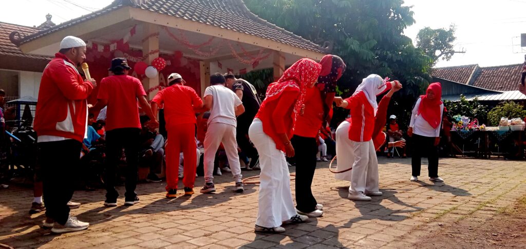IMG_20260816_092851 - Mabur.co Group of people wearing red outfits dancing together at an outdoor celebration with balloons and a decorated stage.