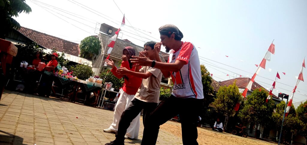 IMG_20260816_101825 - Mabur.co Group of four people dancing in a driveway during a daytime outdoor celebration with red-and-white banners overhead, in a residential area.