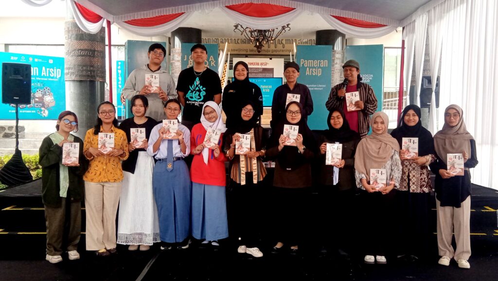 Group of students and organizers on a stage at a book fair, each holding a booklet or program.