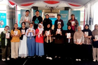 Group of students and organizers on a stage at a book fair, each holding a booklet or program.