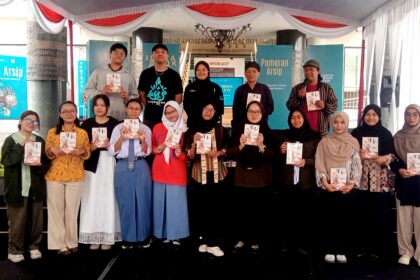 Group of students and organizers on a stage at a book fair, each holding a booklet or program.