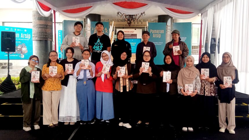 Group of students and organizers on a stage at a book fair, each holding a booklet or program.