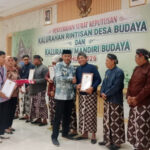 Recipients receive certificates at a cultural village awards ceremony, with a banner in Indonesian in the background.