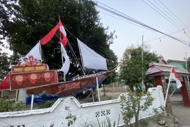 Decorated parade boat or float with red and white fabric on a residential street, trees in the background and a white wall fence nearby
