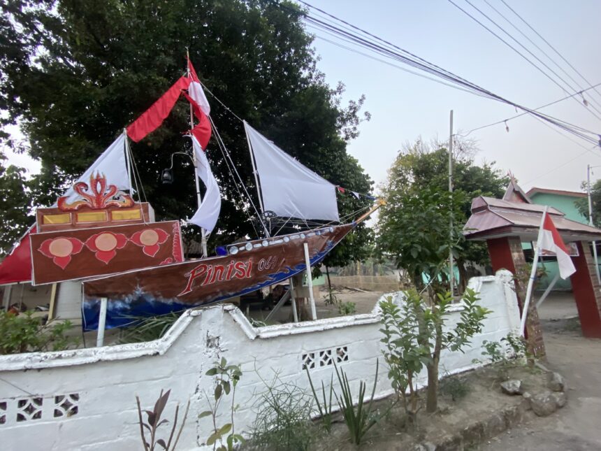 Decorated parade boat or float with red and white fabric on a residential street, trees in the background and a white wall fence nearby