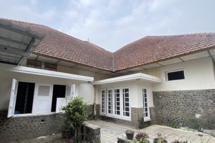Courtyard view of a house with red-tiled pitched roofs, white doors, and stone-clad lower walls with potted plants.