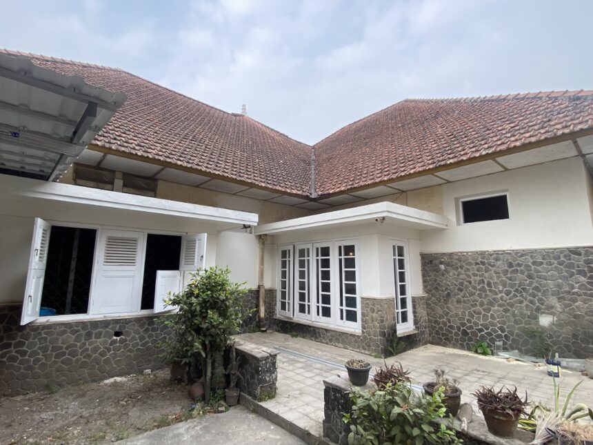Courtyard view of a house with red-tiled pitched roofs, white doors, and stone-clad lower walls with potted plants.