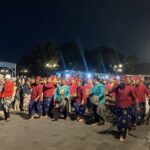 Nighttime street parade with performers in red and blue traditional outfits carrying drums and fans.