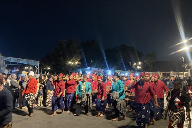 Nighttime street parade with performers in red and blue traditional outfits carrying drums and fans.